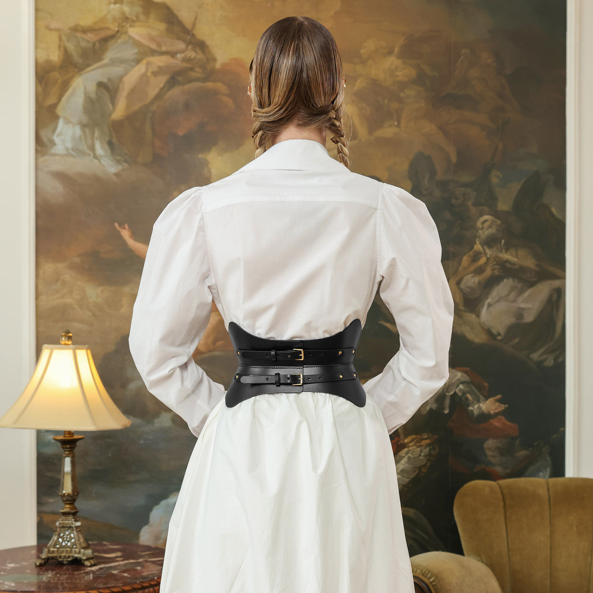 Person wearing a white shirt with a black belt in front of a large painting
