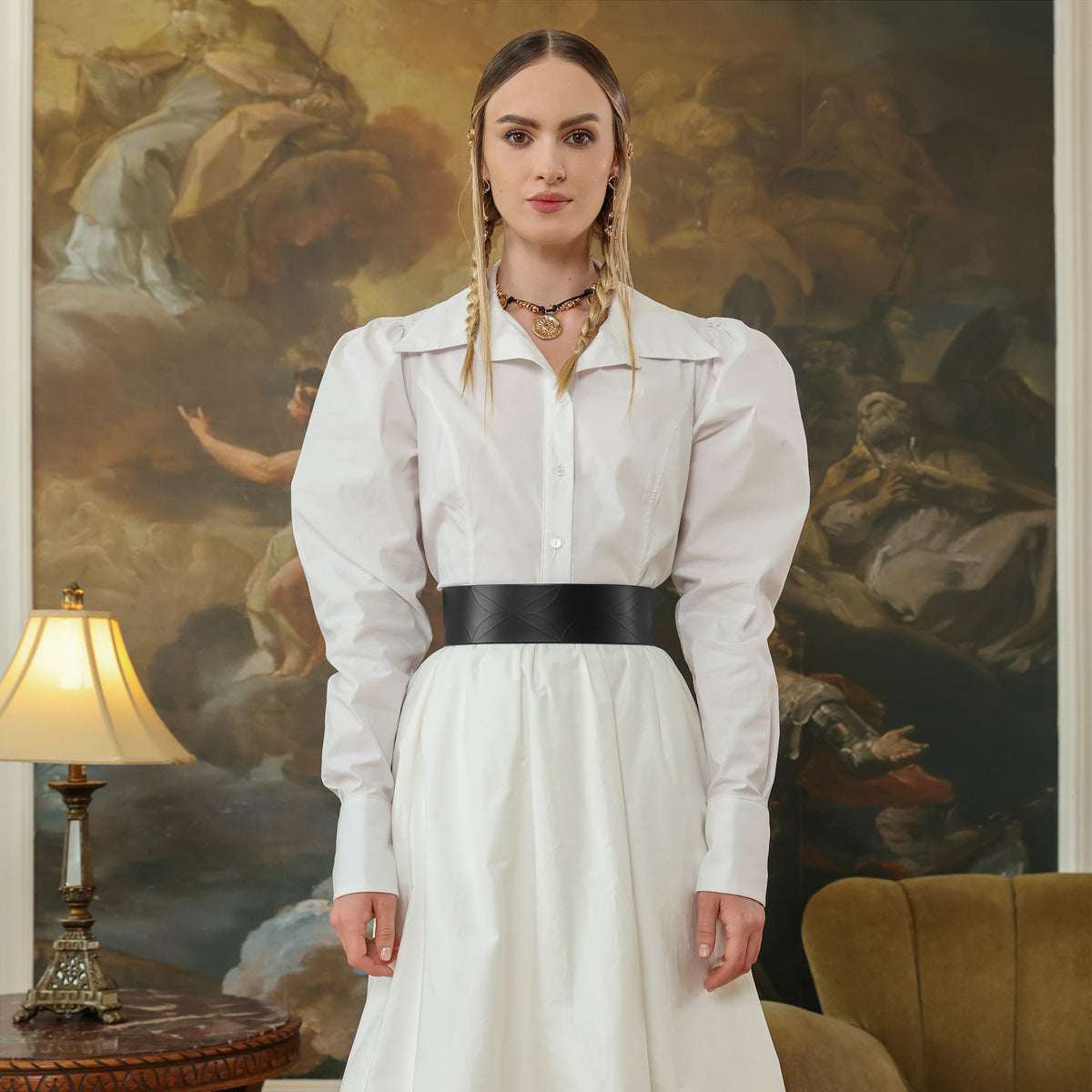 Woman in a white dress with a black belt standing in front of a large painting.