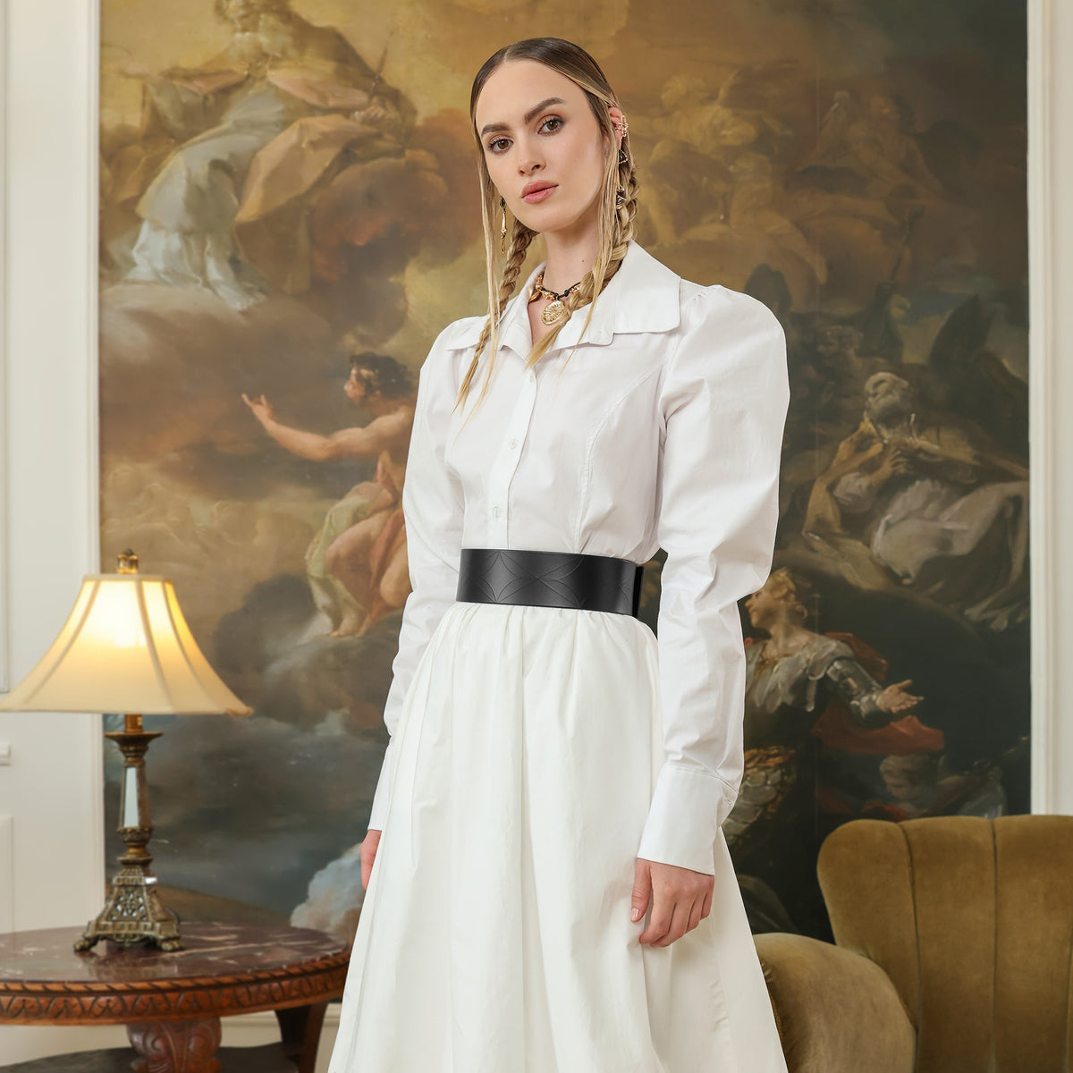 Woman in a white dress standing in a room with classical painting in the background