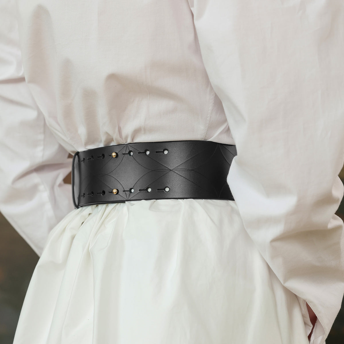 Person wearing a white shirt with a black belt featuring gold studs.