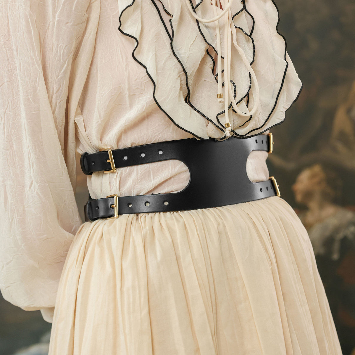 Person wearing a black belt with gold hardware on a neutral background