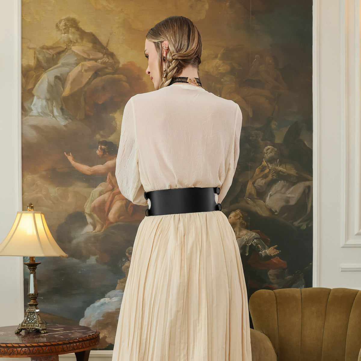 Woman in a beige dress standing in a room with classical painting on the wall.