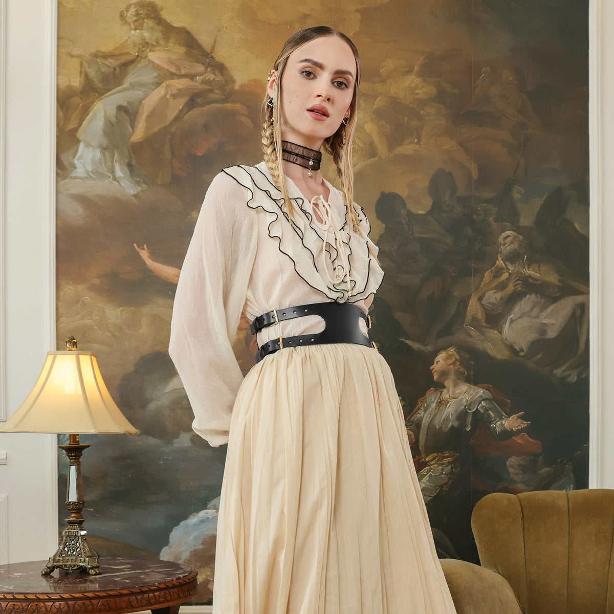 Woman in a white blouse and beige skirt standing in front of classical painting