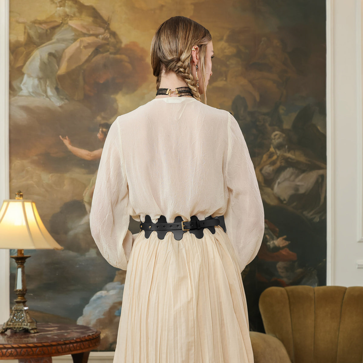 Woman in a beige dress standing in a room with a large painting on the wall.