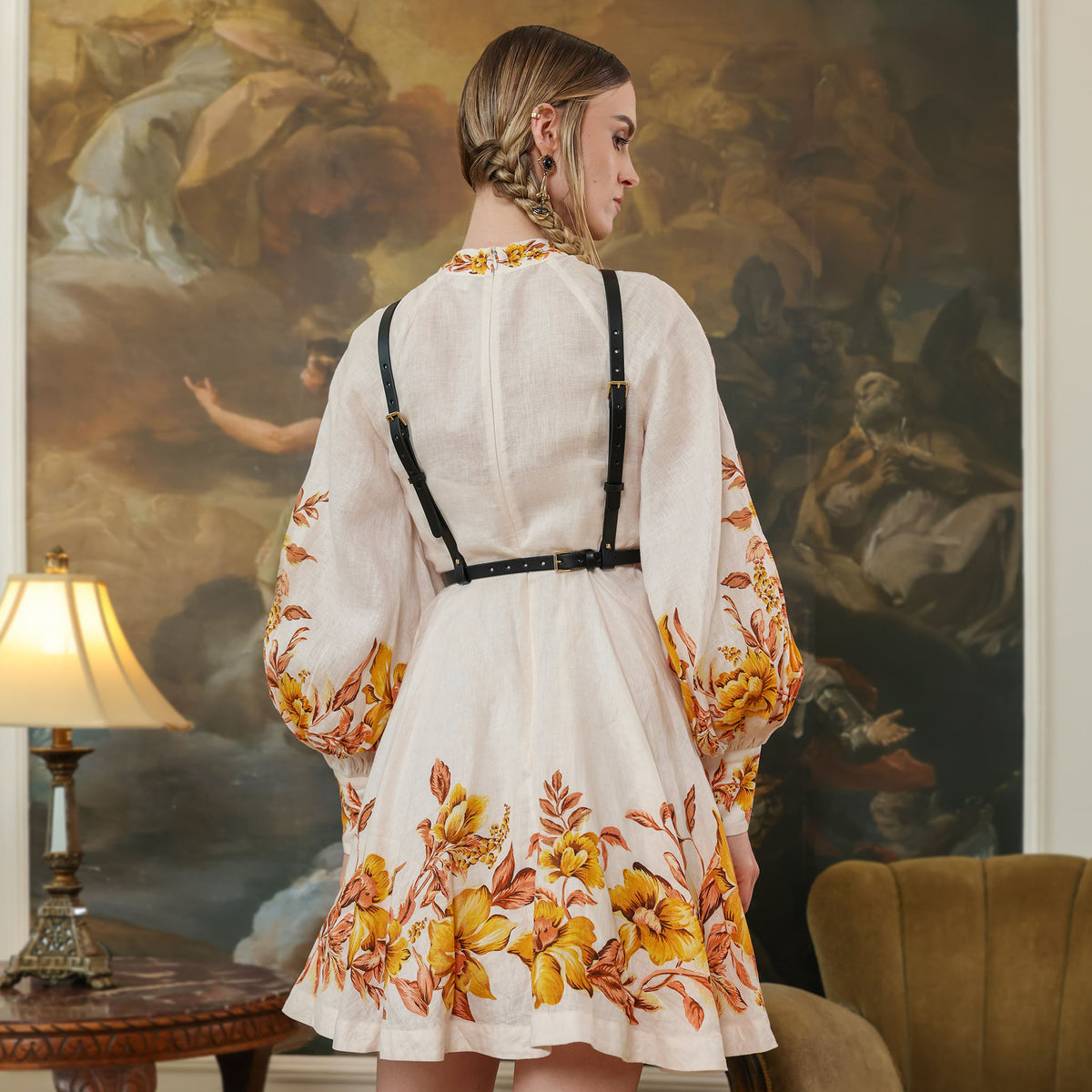 Woman wearing a white dress with floral patterns in a room with a large painting on the wall.