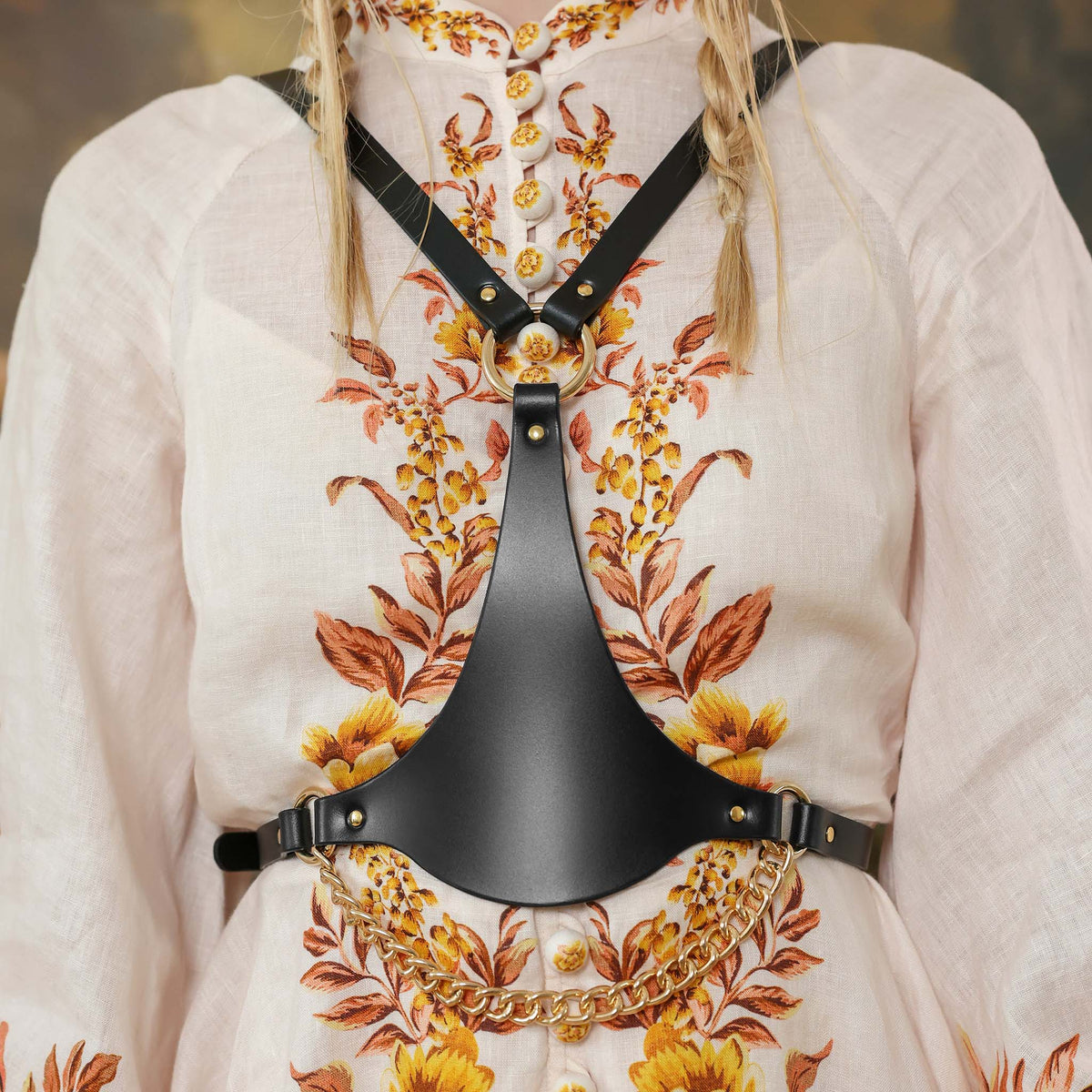 Person wearing a floral-patterned garment with a black leather harness over it.
