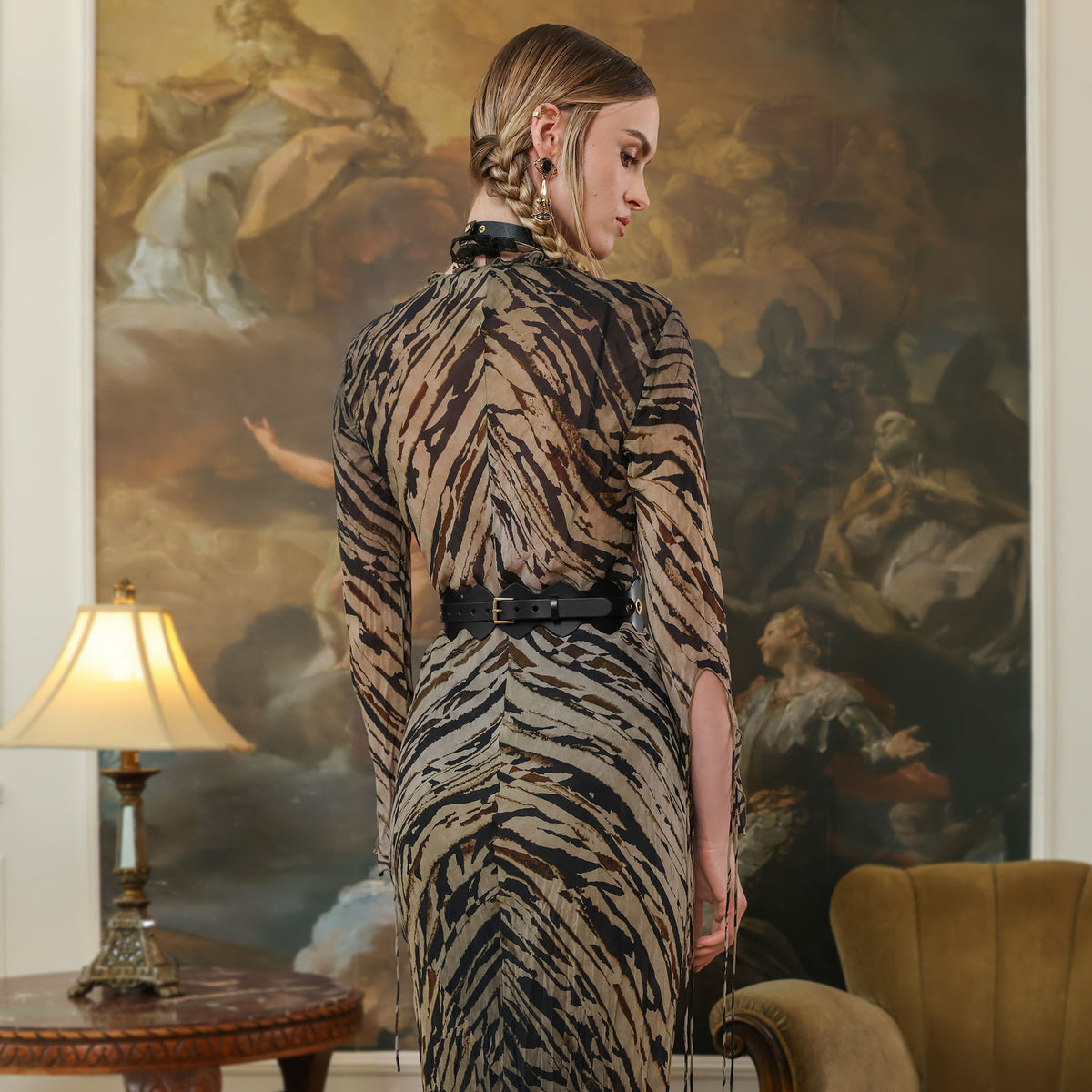 Woman in a zebra print dress standing in a room with a large painting on the wall.