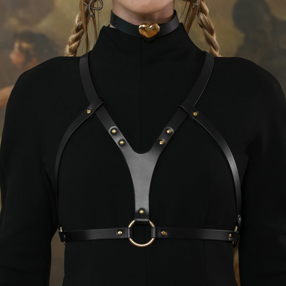 Black leather harness with gold accents worn by a person, with a blurred background