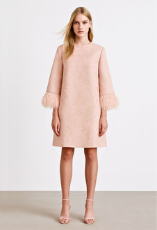 Model wearing powder pink mini dress with feather trim cuffs.