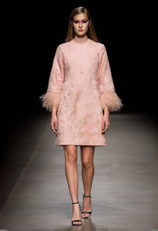 Model wearing powder pink mini dress with feather trim cuffs.
