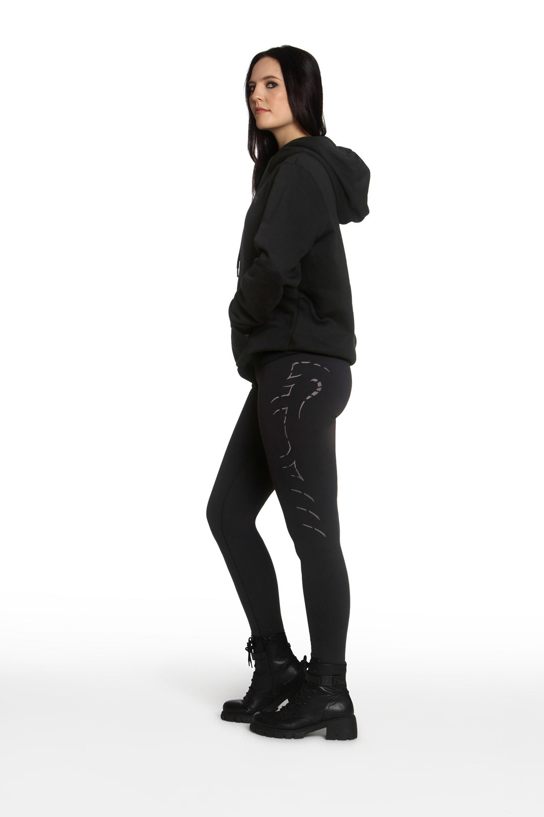 Woman wearing a black hoodie and black pants with white designs on a white background