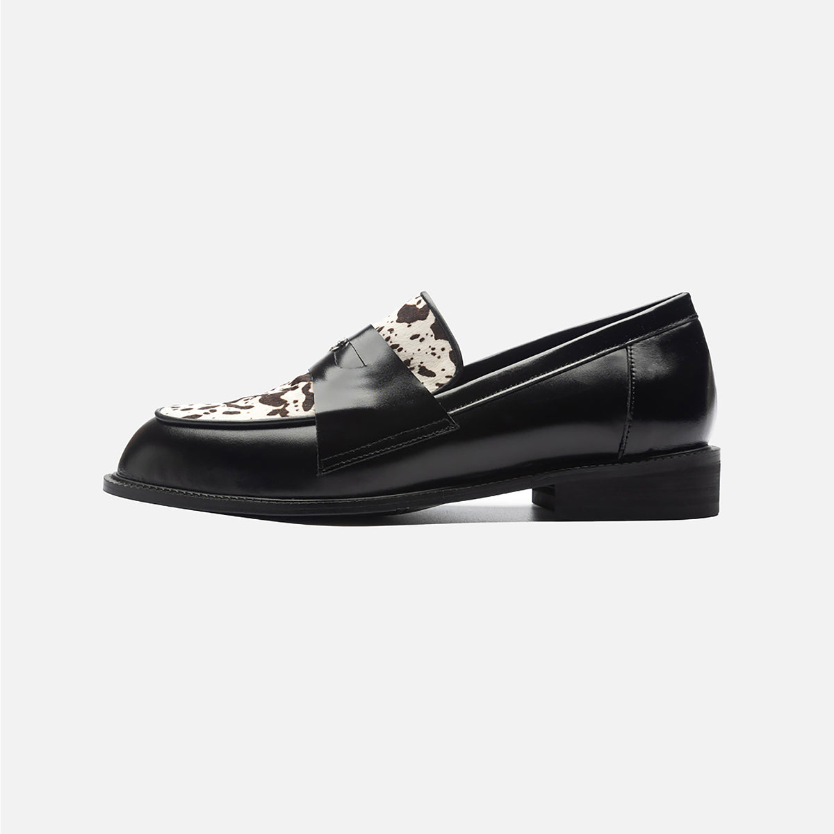 The THEN Black Leather Loafers with Cowhide Print Vamp are handmade in Korea, featuring a low heel and a striking black and brown cowhide-print vamp, displayed in profile against a plain white background.