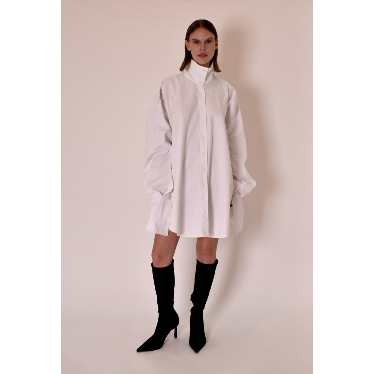 Person wearing a white dress with a high collar against a plain background