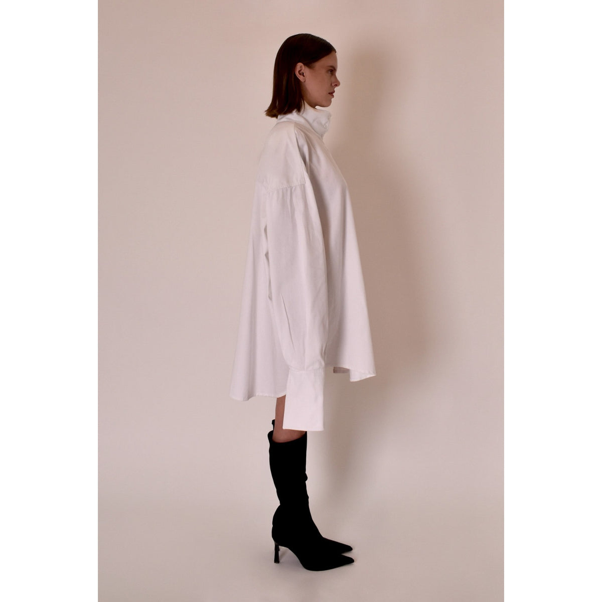 Person wearing a white oversized shirt and black boots against a plain background