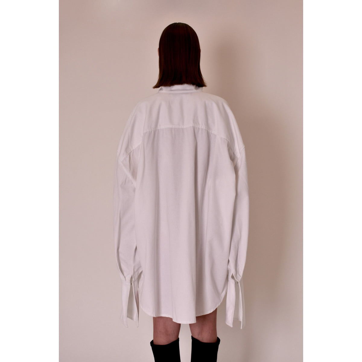 Person wearing a white oversized shirt against a plain background