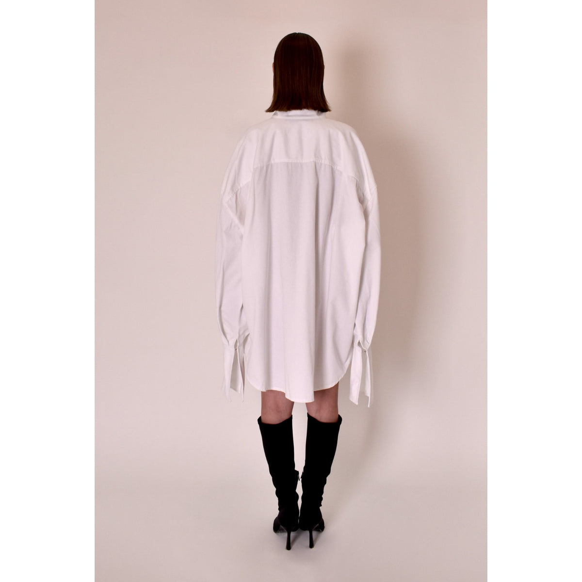 Person wearing a white oversized shirt against a plain background