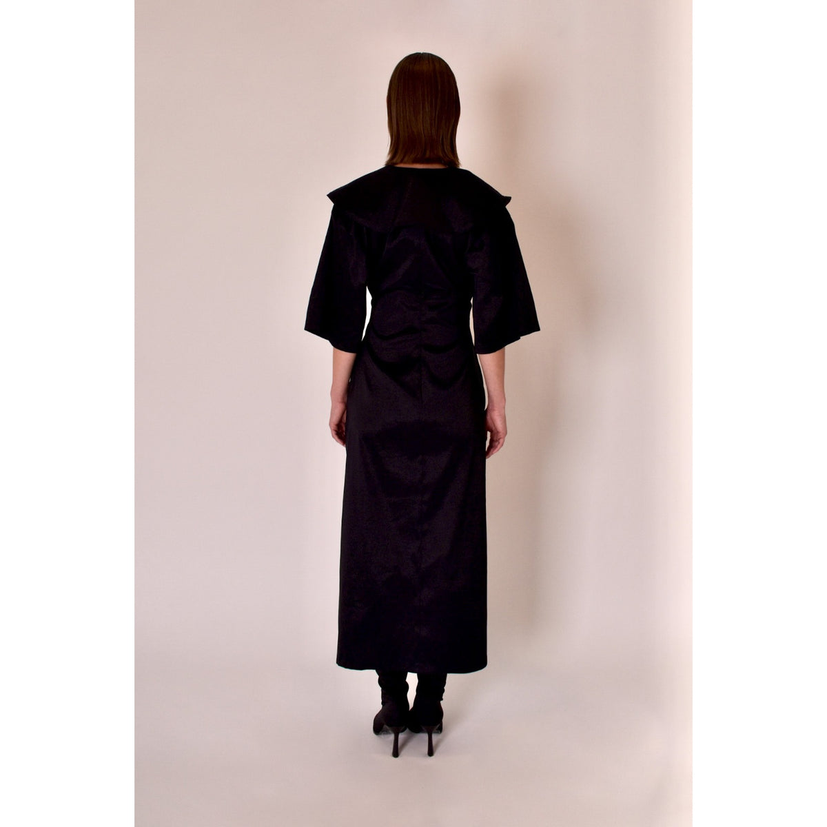 Person wearing a black dress standing against a plain background