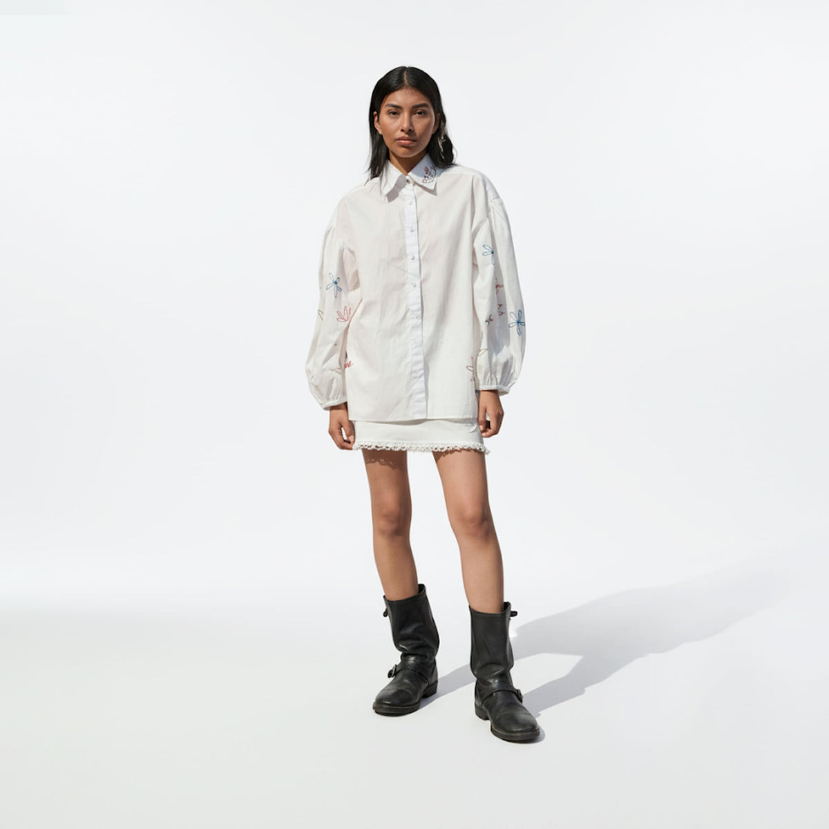 Person wearing a white oversized shirt and black boots on a white background