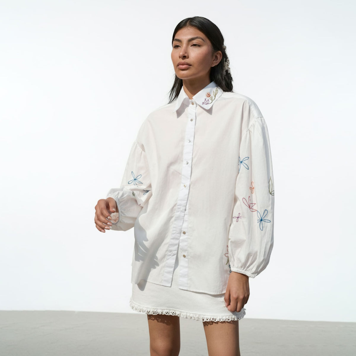 Woman wearing a white embroidered shirt with colorful designs on a plain background