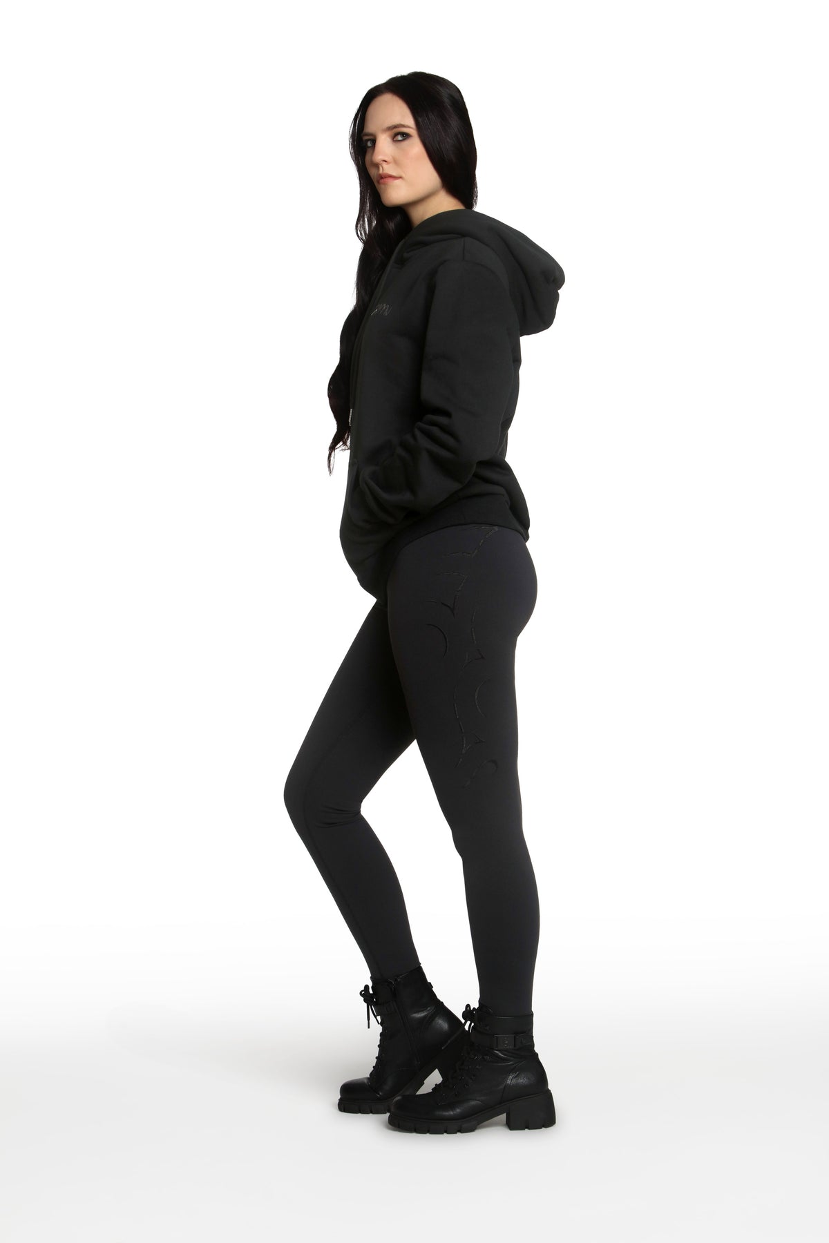 Person wearing a black hoodie, leggings, and boots on a white background