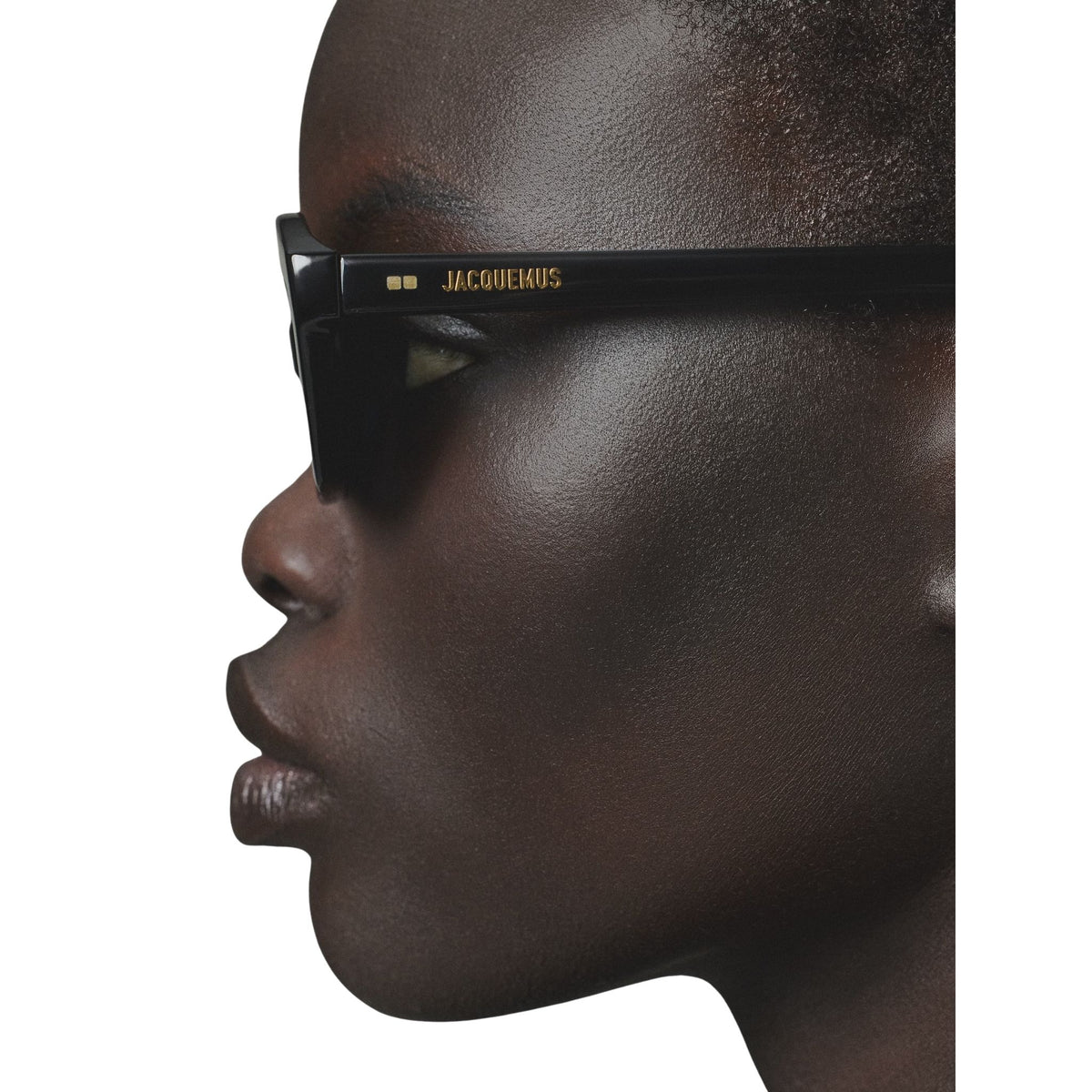 Side view of a person wearing black sunglasses with 'Jacquemus' branding on a white background