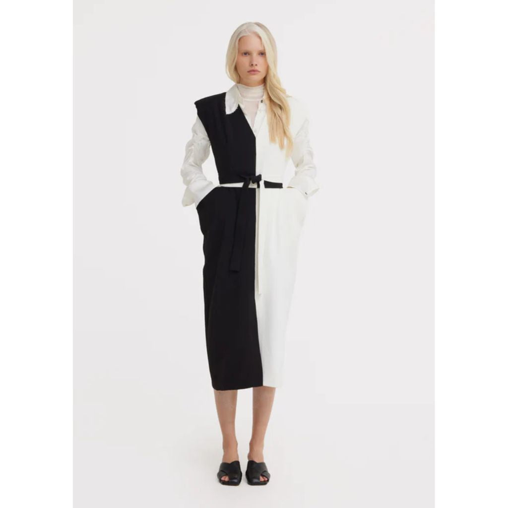 A woman with long, blond hair stands against a white background wearing the JULIA ALLERT Fashion Midi Dress With Belt And Bold Shoulders – Black &amp; Ivory, featuring a wide collar and her hands resting casually in the dress’s pockets.