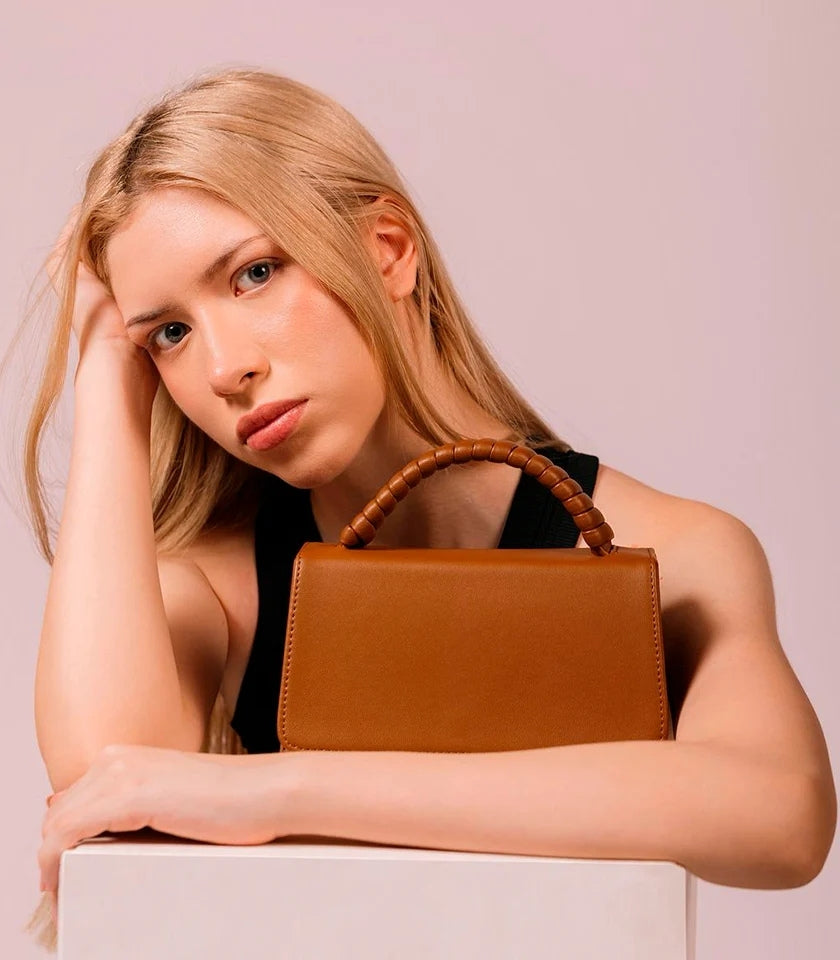 Woman holding a brown handbag against a plain background