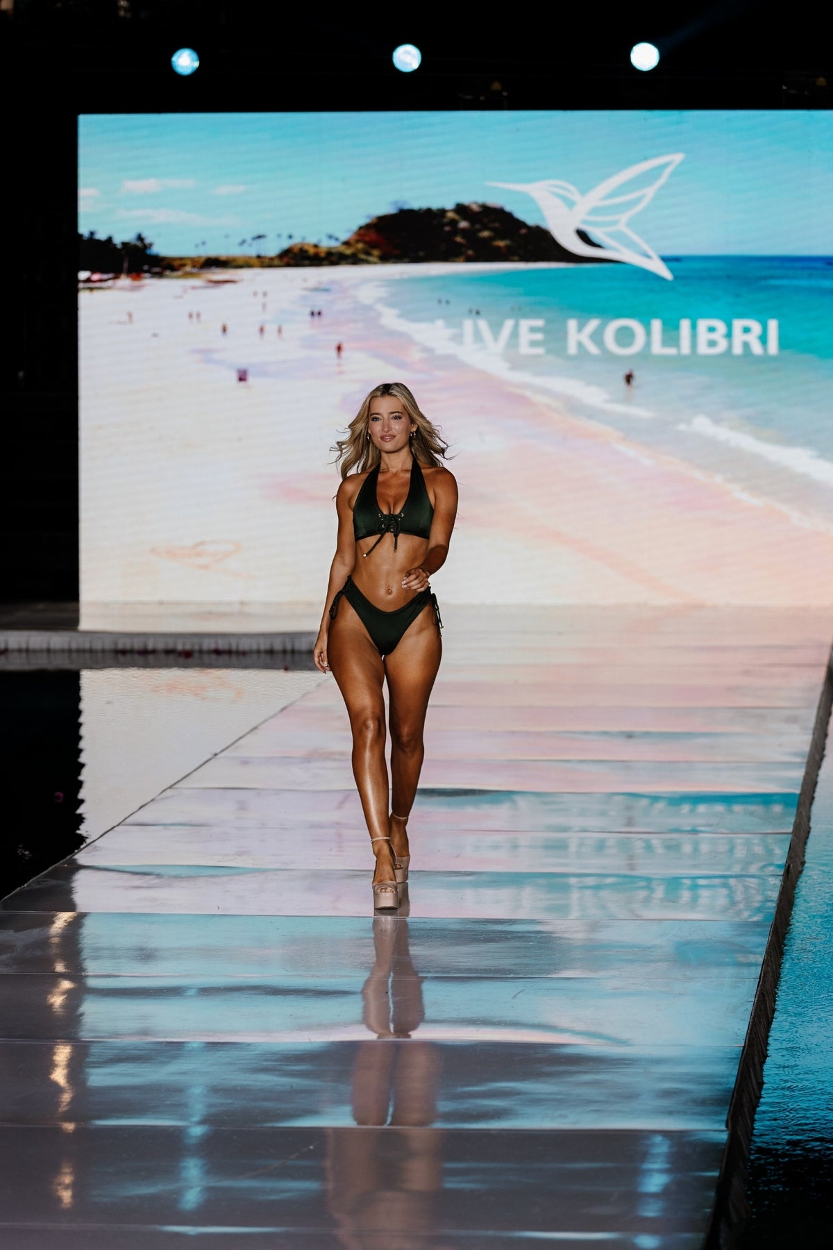 Model wearing forest green lace-up bikini set with gold accents