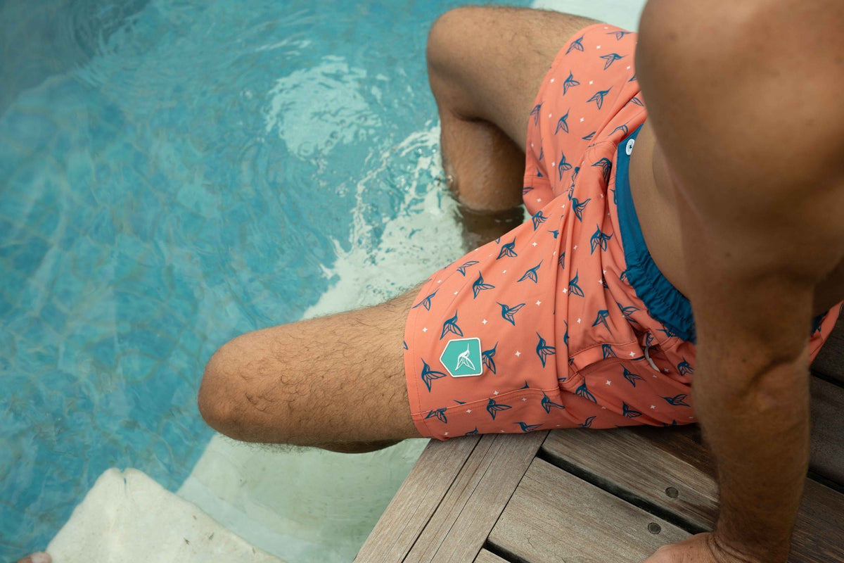 Model wearing Sunset Orange monogram swim trunks poolside