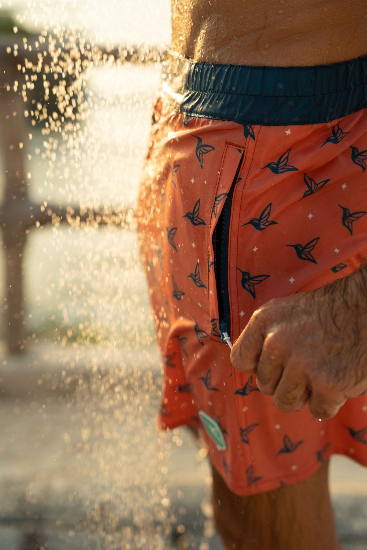 Model wearing Sunset Orange monogram swim trunks poolside