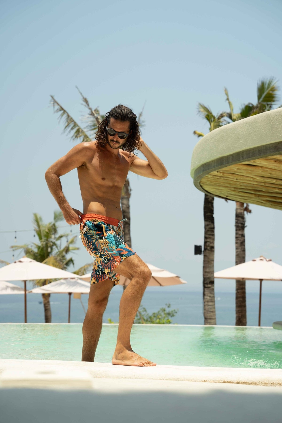 Model wearing eco-friendly jungle print swim shorts by resort pool
