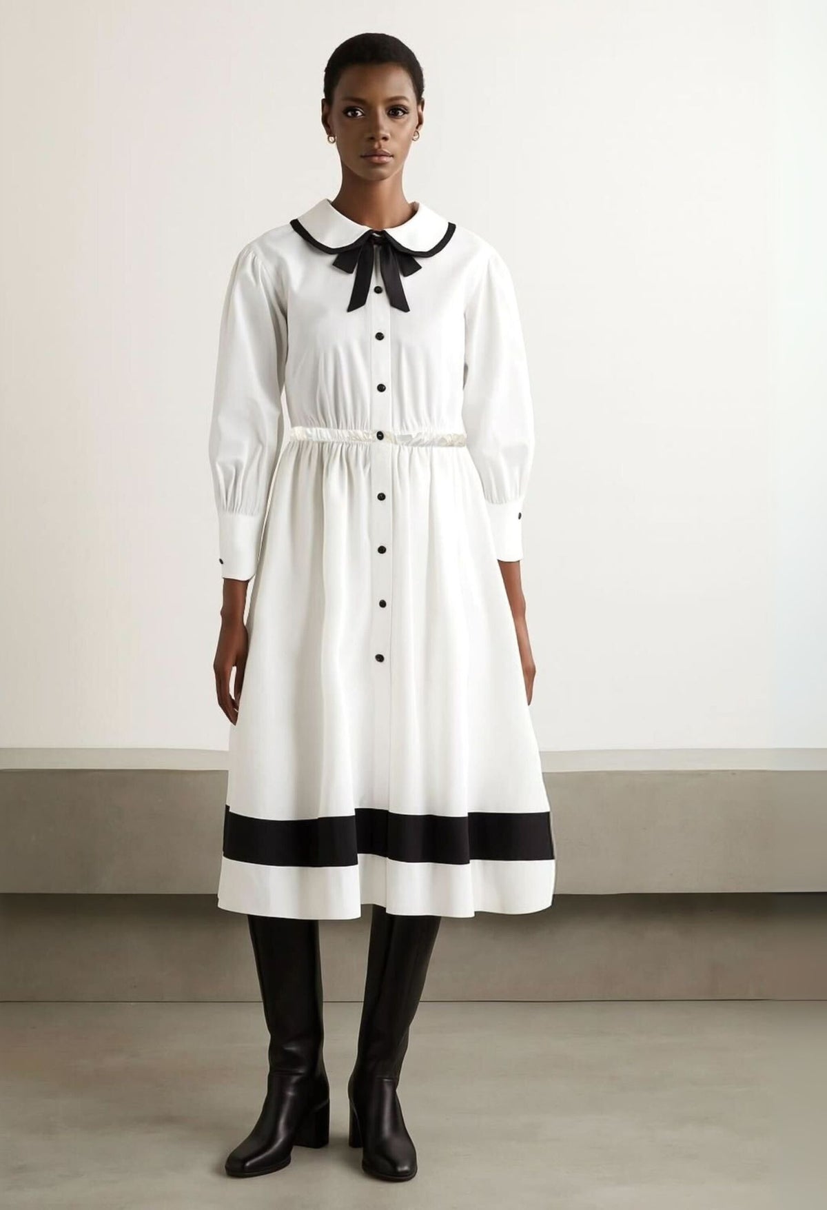 Model wearing white long sleeve shirt dress with black hem stripe and bow collar