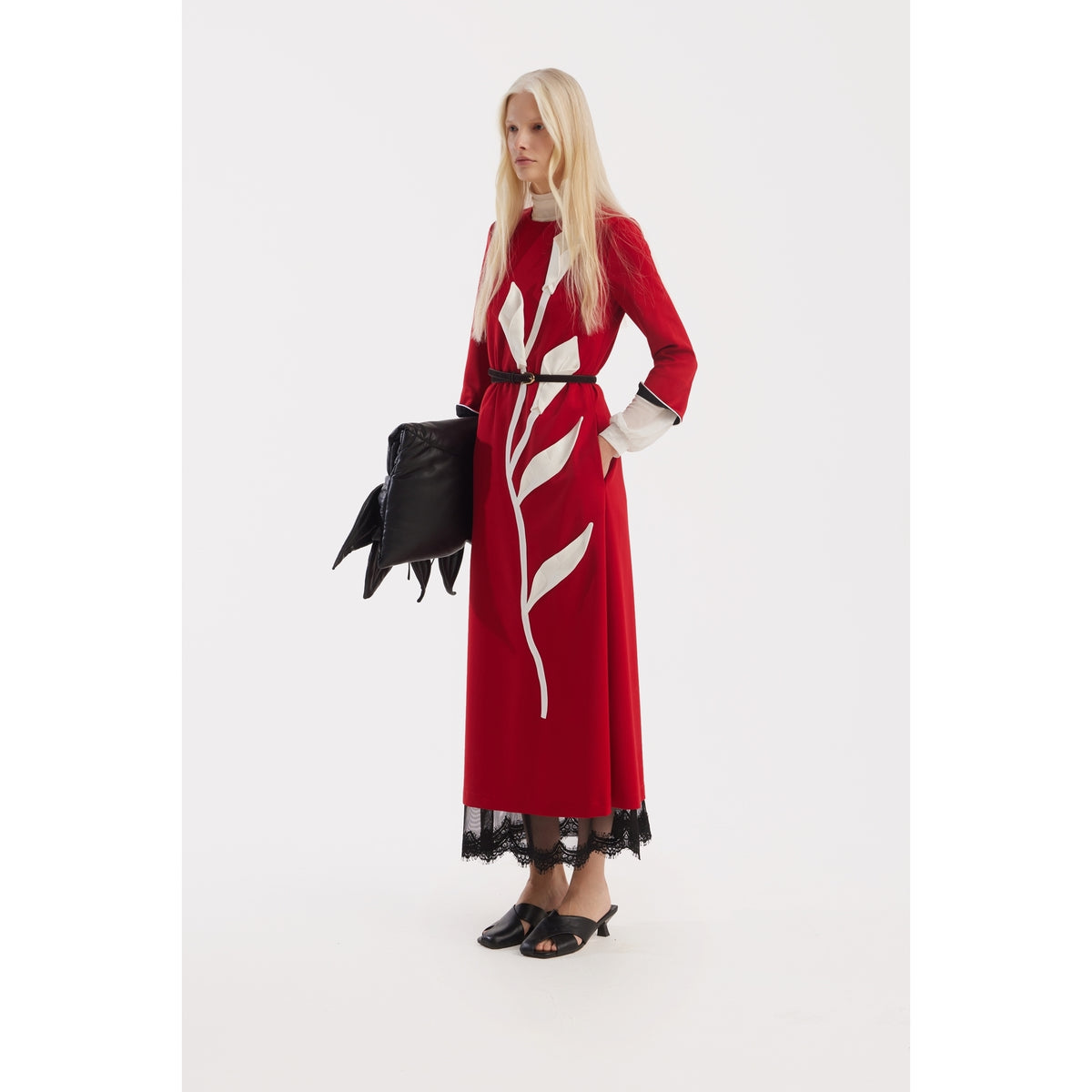 A woman with long blonde hair wears the Art-Inspired Semi-Fitted Three-Quarter Sleeves Dress in red by JULIA ALLERT, holding a large black hand-shaped clutch against a plain white background.