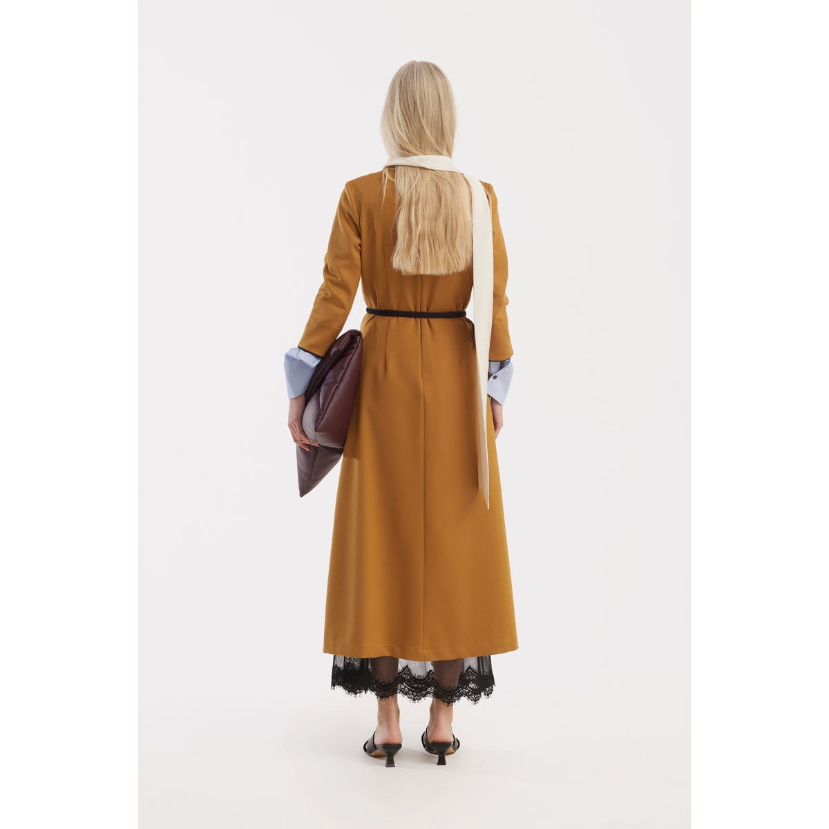 A woman with long blonde hair, seen from behind, wears a mustard Art-Inspired Semi-Fitted Three-Quarter Sleeves Dress by JULIA ALLERT, paired with a white scarf, black heels, and a dark brown clutch against a white background.