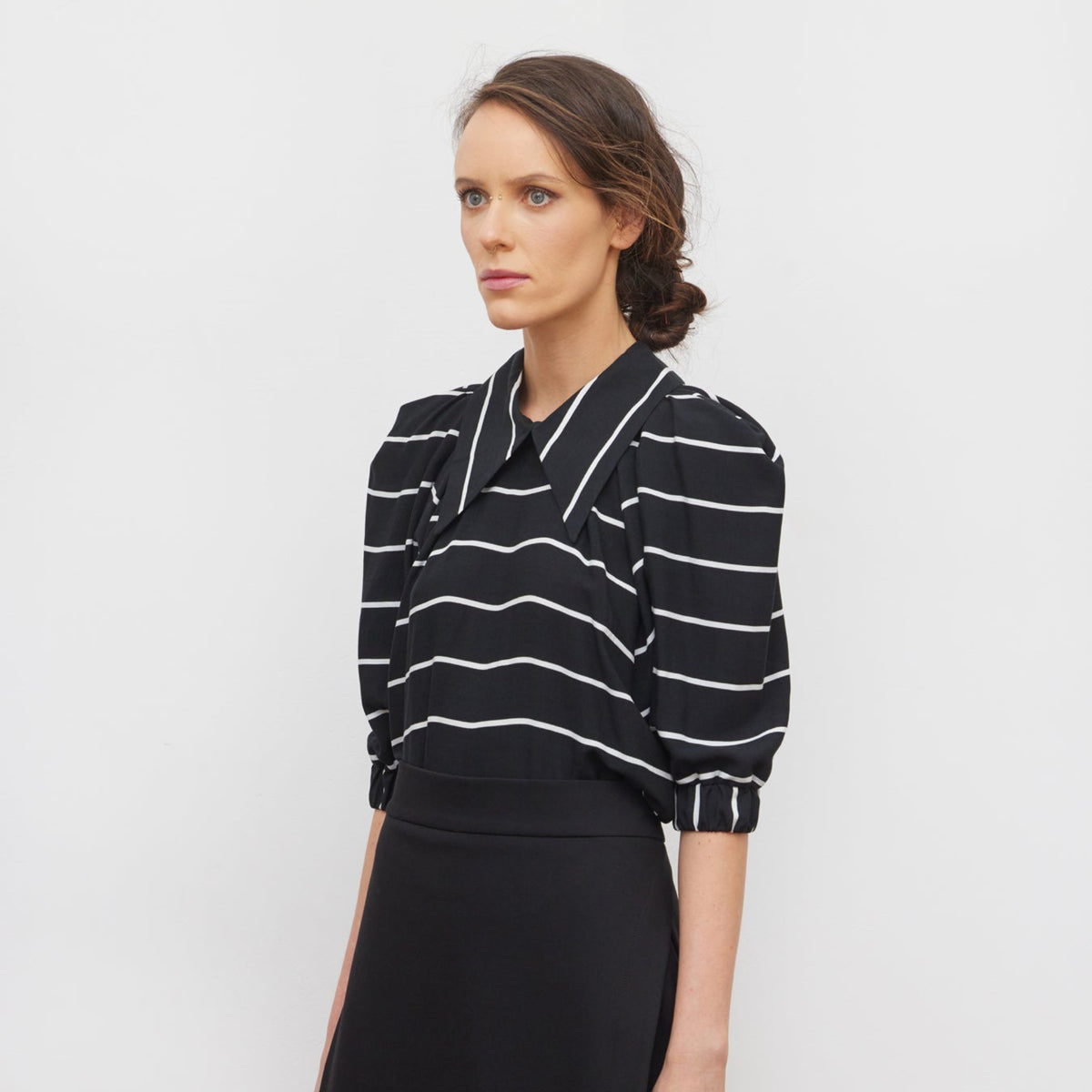 Woman wearing a black and white striped shirt and black skirt on a white background