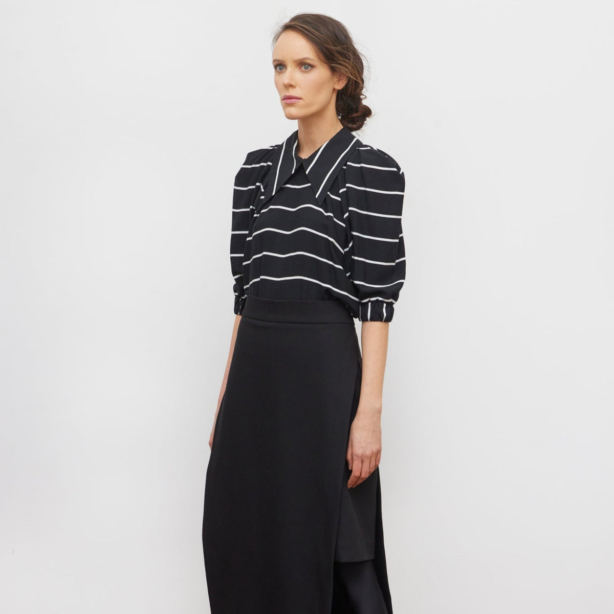 Woman wearing a black and white striped shirt with a black skirt on a white background