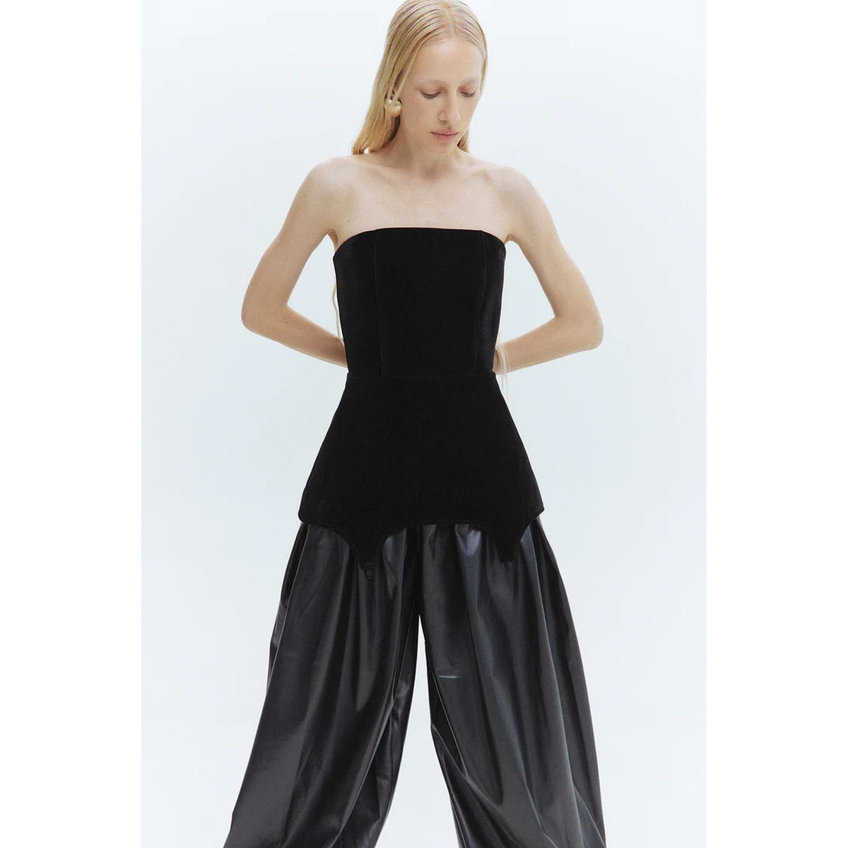 Woman wearing a black strapless top and black wide-leg pants on a white background