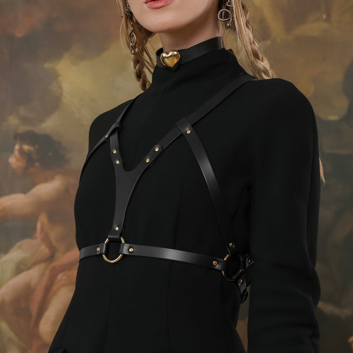 Person wearing a black outfit with leather straps against a classical painting background